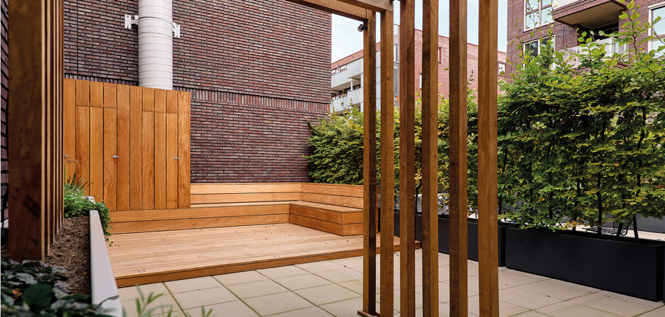 Houten zitbank en lamellen tegen bakstenen muur op dakterras in Rotterdam