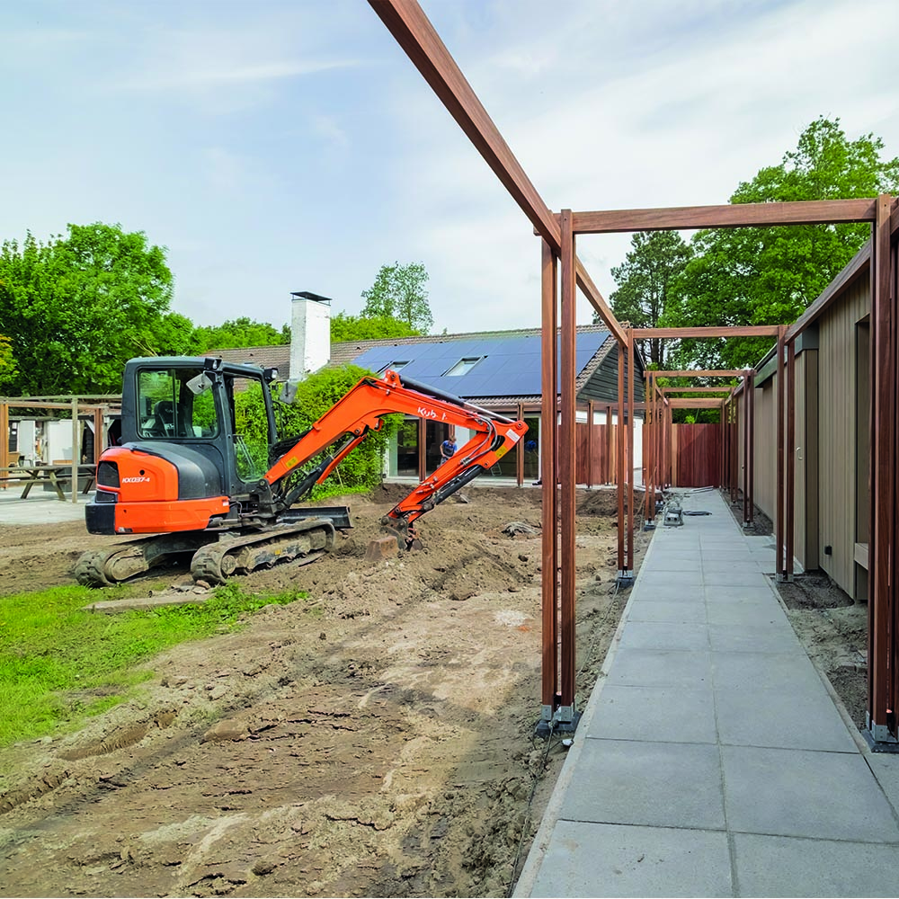 Minigraver naast houten pergola en tegelpad in Oud-Beijerland